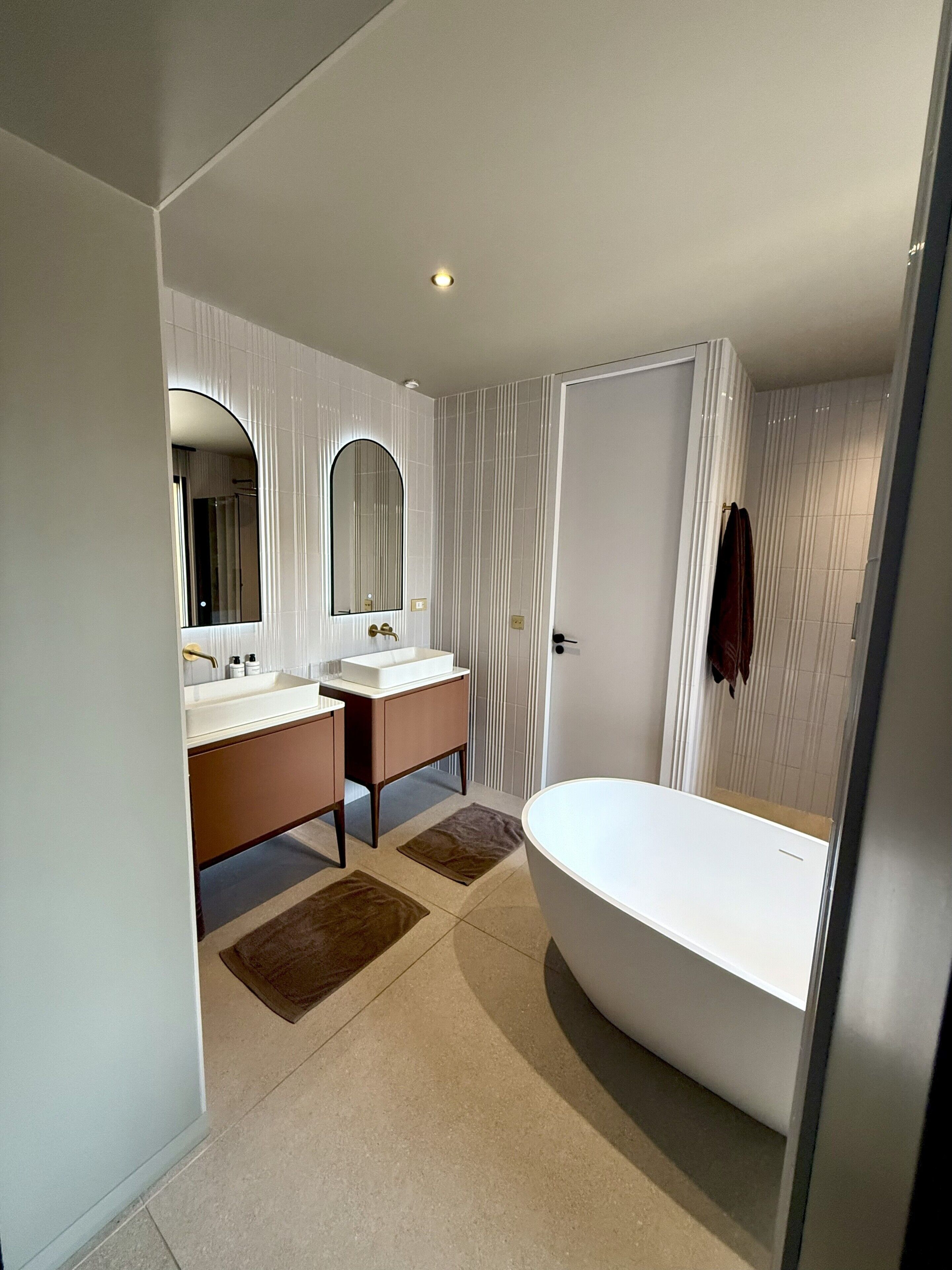 A modern bathroom with a double sink, a large bathtub, and a mirror.