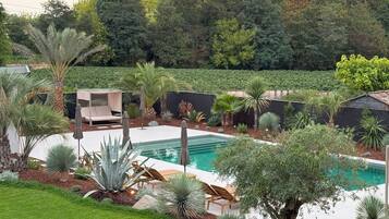 Un área de piscina con sillones de descanso y una pequeña terraza, rodeada de plantas y árboles.
