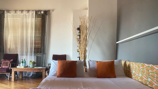 A hotel room with a large bed, two orange pillows, a wooden table with bottles, a chair, and a vase with tall reeds. - Luxury Retreat in Franciacorta (Villa Pedergnano)