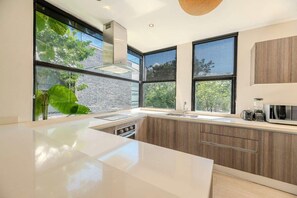 A modern kitchen with a large island, a built-in stove, and a window overlooking greenery.
