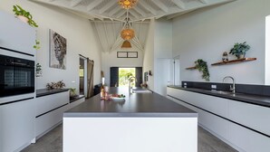A modern kitchen with a central island, white cabinetry, and a large window providing natural light.