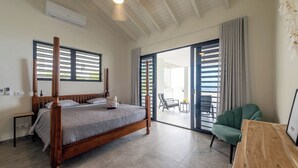 A bedroom with a four-poster bed, a wooden nightstand, a chair, and a view of the outside through a sliding glass door.