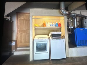 A laundry room with a dryer, a stacked washer, and a shelf with various bottles.