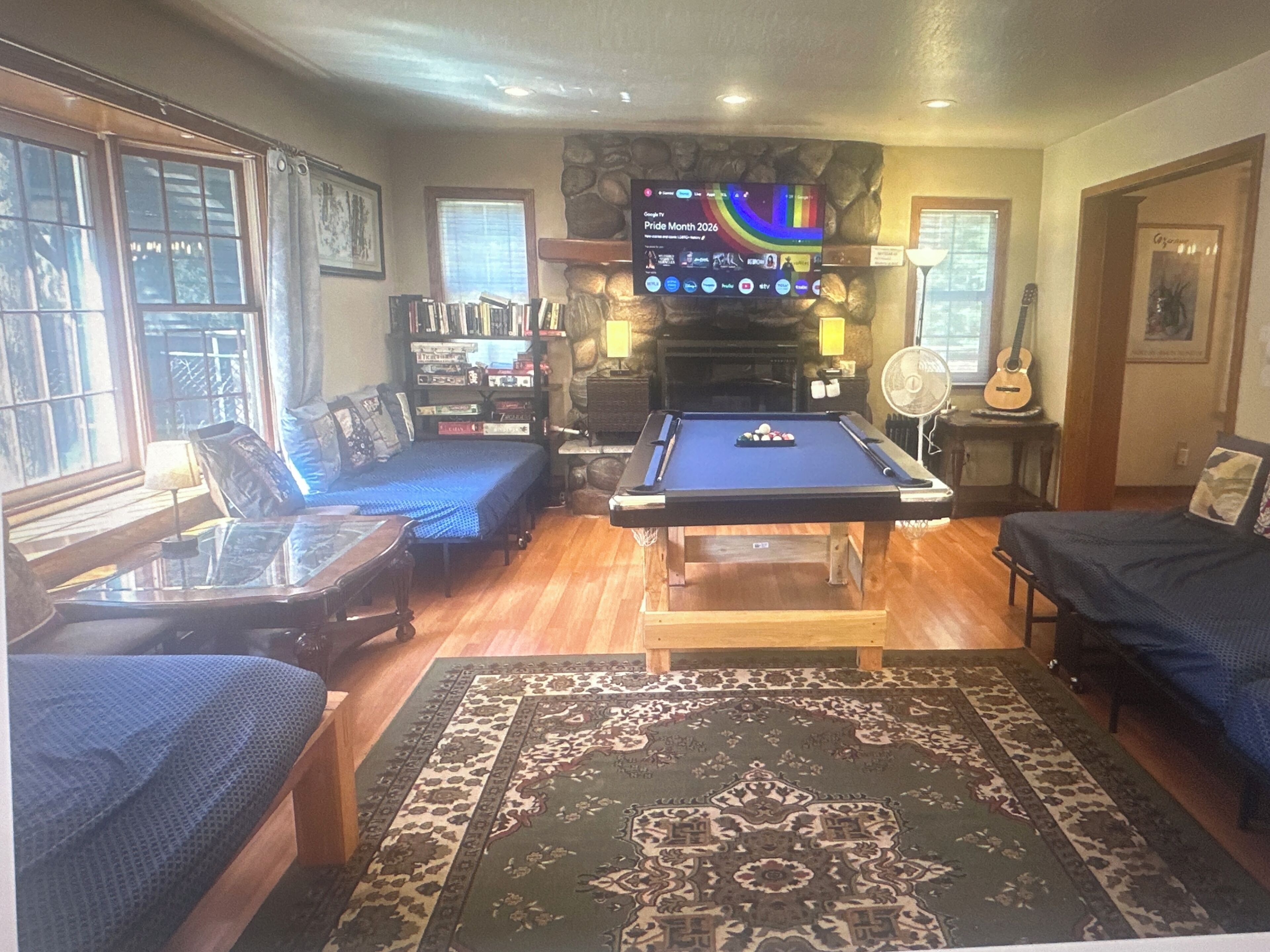 A room with a pool table, a sofa, a bookshelf, and a fireplace.