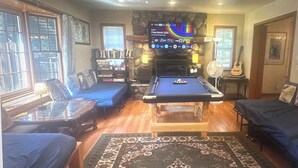 A room with a pool table, a sofa, a bookshelf, and a fireplace.
