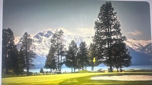 A golf course with a lake and mountains in the background.