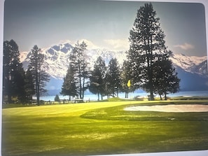 Un campo de golf con un lago y montañas al fondo.