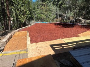 A construction site with a large area covered in red mulch, surrounded by trees and a wooden platform.