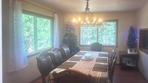 A dining room with a table set for four, a chandelier, a Christmas tree, and a television on a stand.