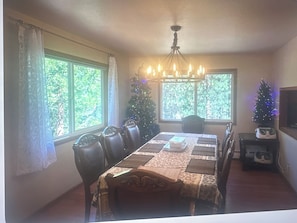 Un comedor con una mesa preparada para cuatro personas, una araña, un árbol de Navidad y un televisor sobre un soporte.