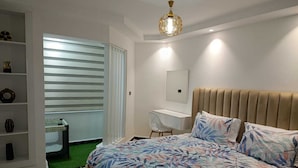 A bedroom with a bed, a desk, a chair, a wardrobe, and a window with blinds.