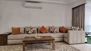 Ein Wohnzimmer mit einer Couch, einem Couchtisch, gemusterten Kissen und einem Fenster mit Jalousien.