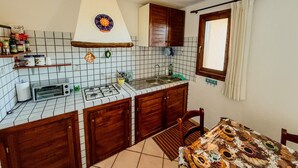 Cocina compacta con salpicadero de azulejos, armarios de madera, horno empotrado y comedor con mantel estampado.