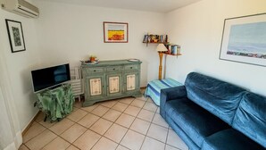 Una sala de estar con un televisor sobre un mueble bajo, un armario verde, un sofá azul y una estantería.