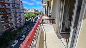 A balcony with a red railing overlooking a street with parked cars and buildings.