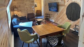 Hyggelig interiør i en træhytte med sofa, spisebord, stole, fjernsyn og pejs.