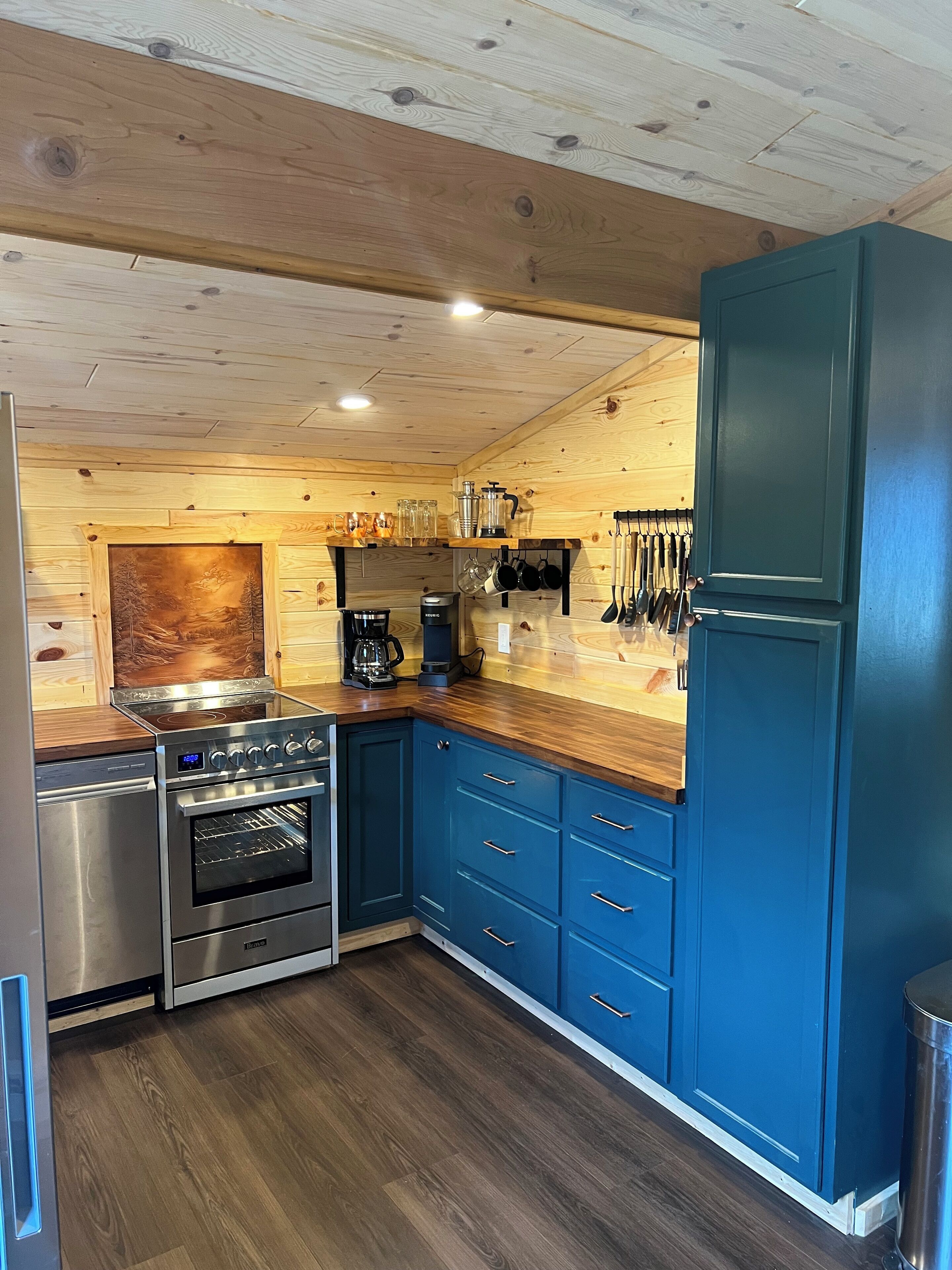 A modern kitchen with wooden cabinetry, stainless steel appliances, and a blue accent wall.