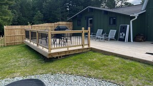 En terrasse med udendørs møbler, grill og et hus med grøn facade.