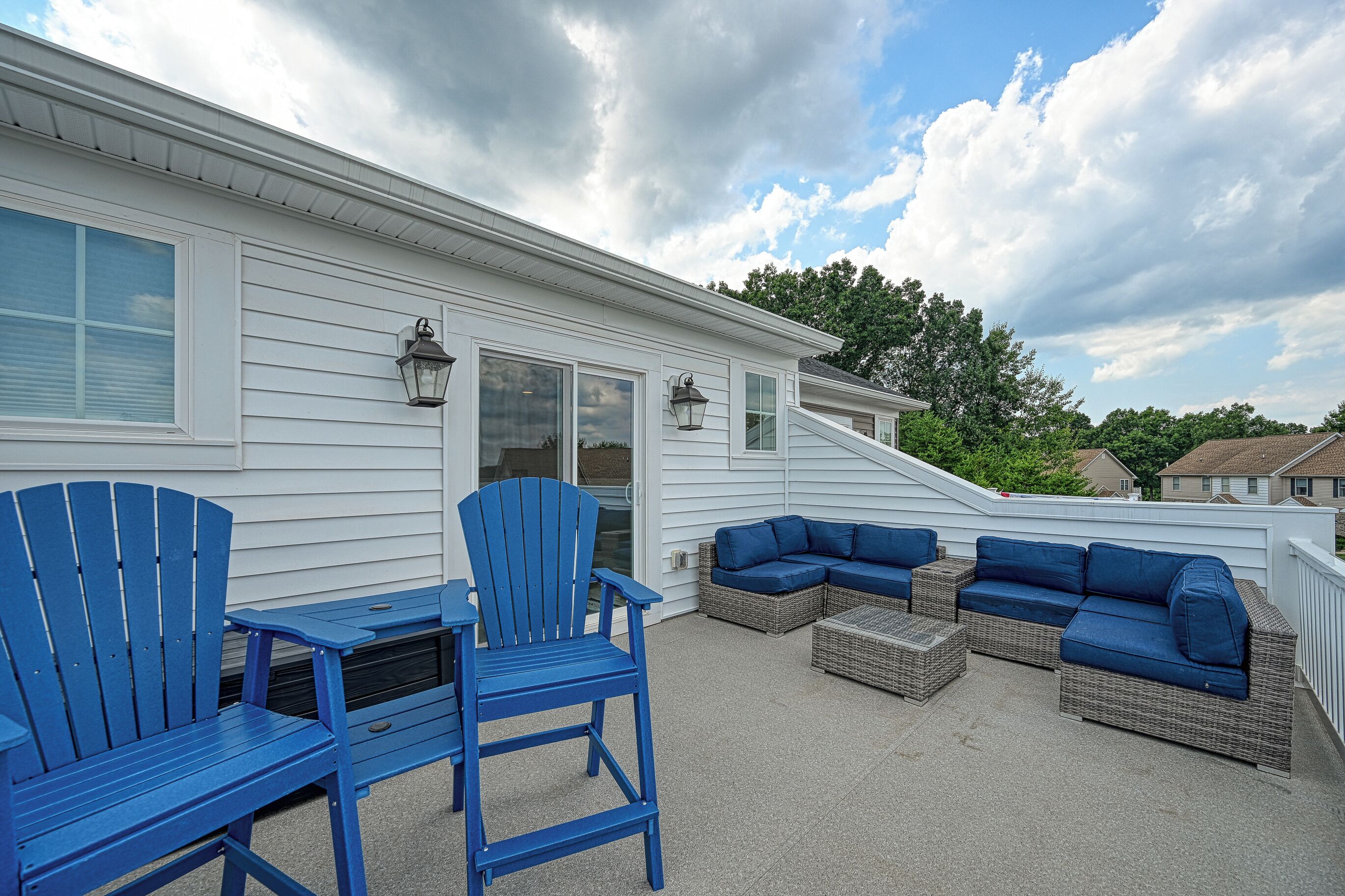 Une terrasse couverte avec des fauteuils Adirondack bleus, un canapé en osier et une petite table.