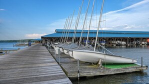 Un muelle de madera que lleva a un muelle techado para barcos con varios veleros amarrados.