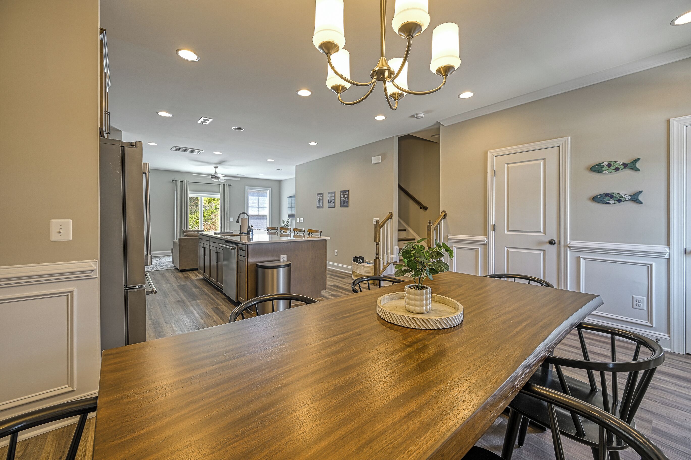 A spacious kitchen with a wooden dining table, recessed ceiling lights, and a chandelier.