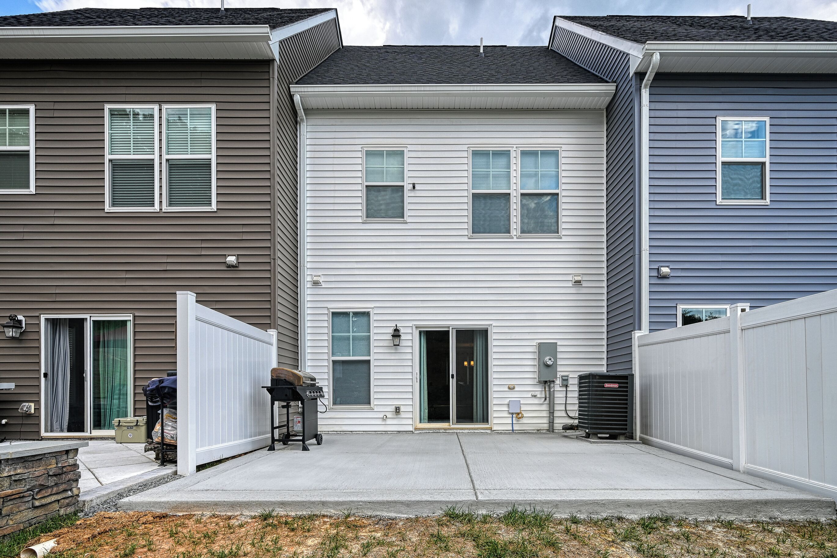 Une rangée de maisons de ville avec une porte centrale, un patio couvert et un espace utilitaire abritant un appareil de climatisation.
