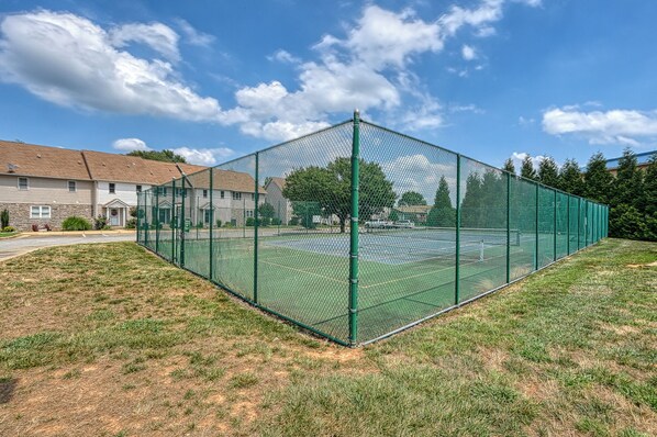 A fenced tennis court with a clear sky and houses in the background.