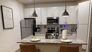 A modern kitchen with white cabinets, stainless steel appliances, and a granite countertop. There are two brown chairs at the island, and a framed inspirational quote on the wall. - Tranquil 2-bedroom apartment in Jacksonville (Jacksonville)