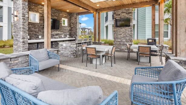 An outdoor patio with stone walls, blue wicker furniture, and a grill area. - Tranquil 2-bedroom apartment in Jacksonville (Jacksonville)