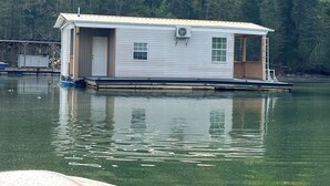 A floating houseboat with a front door, windows, and an air conditioning unit. - Charming 2-bedroom house boat in Norris Lake. (Speedwell)