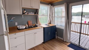A modern kitchen with wooden flooring, white and blue cabinets, a wooden ceiling, and a view of a lake through large windows. - Charming 2-bedroom house boat in Norris Lake. (Speedwell)