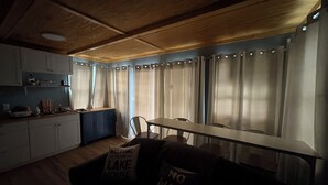 A cozy living area with a wooden ceiling, a dining table, a sofa with pillows, and a kitchen in the background. - Charming 2-bedroom house boat in Norris Lake. (Speedwell)
