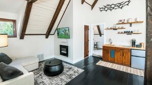 Un interior moderno con techo alto, chimenea, zona de cocina y área de descanso con mesa redonda y sofá.
