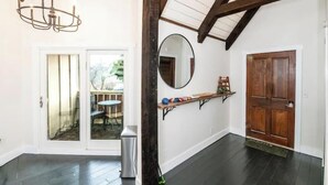 Una habitación con puerta de madera, un espejo, una estantería con objetos y vistas al exterior a través de una puerta de cristal.