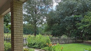 Un patio couvert agrémenté d’un pilier en briques, de plantes en pot et d’un jardin où poussent différentes fleurs et arbustes.