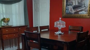 Une salle à manger avec une table et des chaises en bois, un lustre, un tableau et une porte.