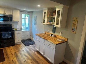 Una cocina con armarios blancos, encimera de madera, microondas y refrigerador.
