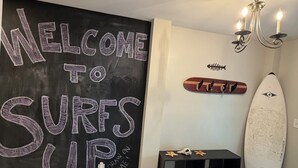 Una habitación con pared de pizarra, una tabla de surf, una araña y un tapete estampado.