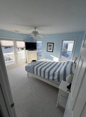A bedroom with a bed, a TV, a ceiling fan, and a balcony with a view.
