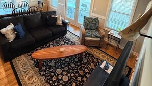 Un salón con un sofá negro, una alfombra estampada, una mesa de centro de madera y un televisor.