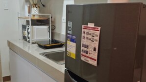 A kitchen with a stainless steel refrigerator, a microwave, and a sink. There are cabinets and a countertop with various kitchen items. - Live the Dream in the Heart of Quezon City! Your Perfect 1-BHK Apartment Awaits. (Quezon City)