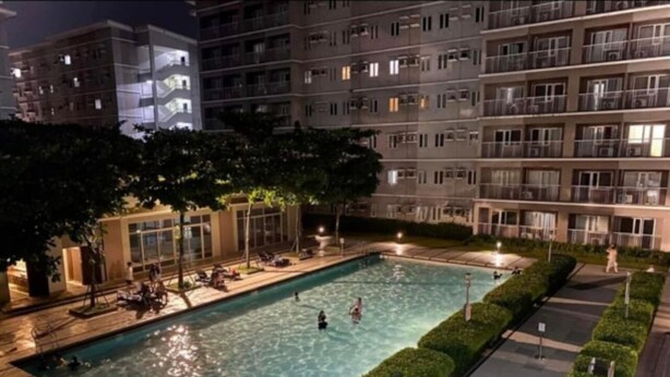 A nighttime swimming pool with people, surrounded by a well-lit building with multiple floors and balconies. - Live the Dream in the Heart of Quezon City! Your Perfect 1-BHK Apartment Awaits. (Quezon City)