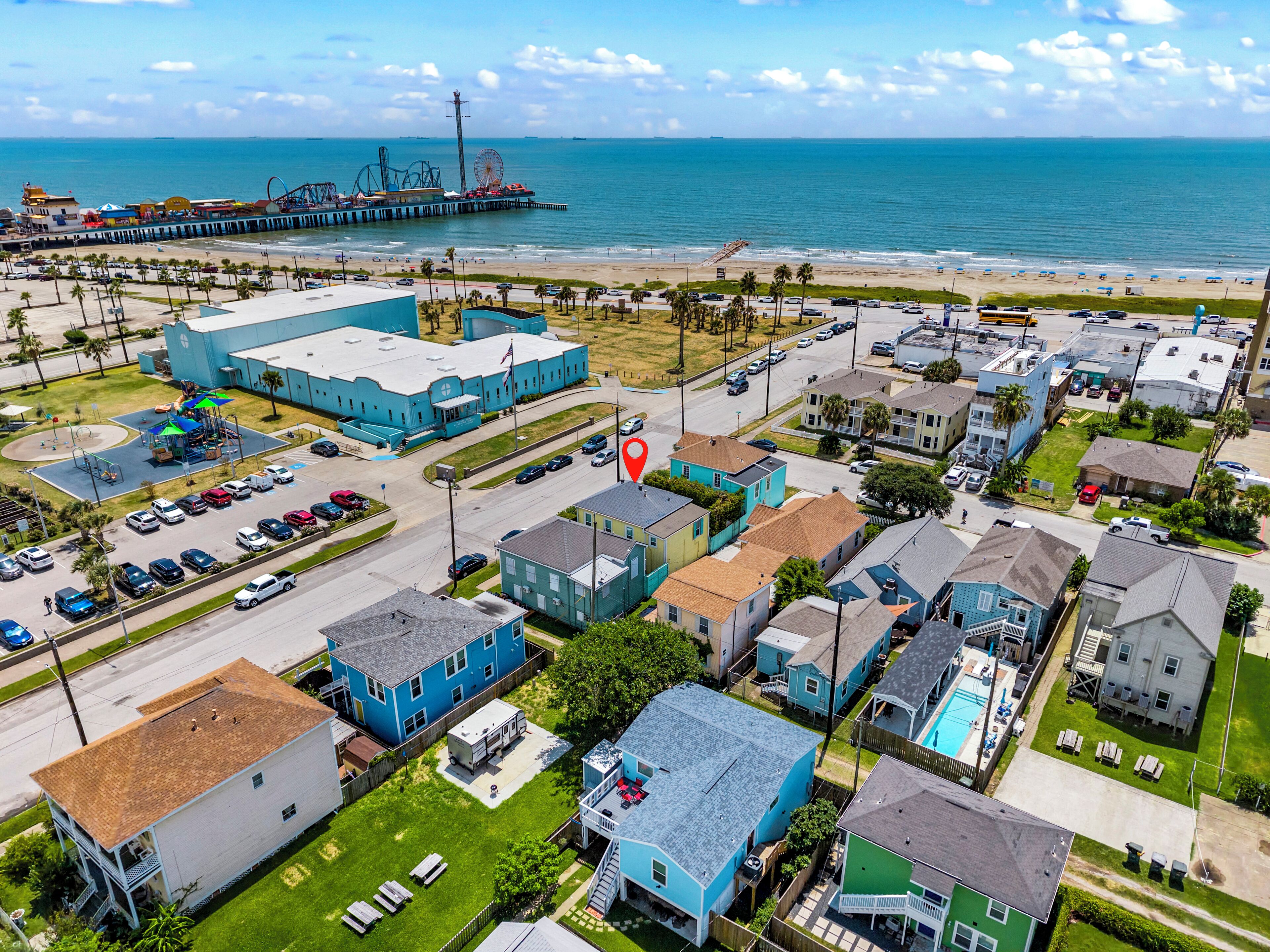 An aerial view of a coastal town with a pier, beachfront, and a mix of residential and commercial buildings.