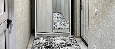Un couloir avec un tapis à motifs, un miroir et un luminaire au plafond.