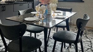 A modern kitchen with dark cabinetry, a gas stove, and a dining area with a glass table set for four. - Chaqar 198 (Tashkent)