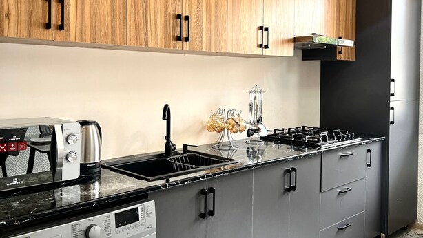 A modern kitchen with wooden upper cabinets, a built-in stove, a sink, and a washing machine. - Chaqar 198 (Tashkent)