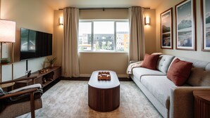 Una sala de estar moderna con una televisión de pantalla plana, una mesa de centro de madera, un sofá y un ventanal con cortinas.