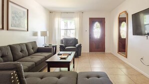 A living room with a sectional sofa, a coffee table, a leather armchair, and a television mounted on the wall. - Inviting home w/ big yard & walkable neighborhood! 3br/2ba (Tampa)