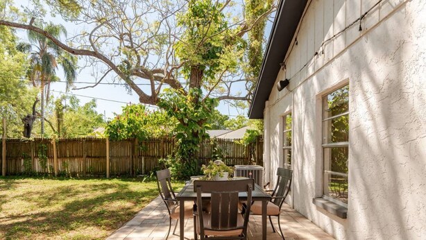 An outdoor patio with a table and chairs, surrounded by a wooden fence and trees. - Inviting home w/ big yard & walkable neighborhood! 3br/2ba (Tampa)