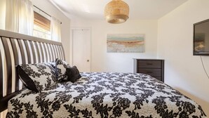 A bedroom with a bed, a bedside table, a lamp, a painting on the wall, and a window with curtains. - Inviting home w/ big yard & walkable neighborhood! 3br/2ba (Tampa)